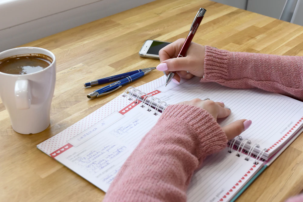 木のテーブルでコーヒーを飲みながら、ノートに書きこむ手元