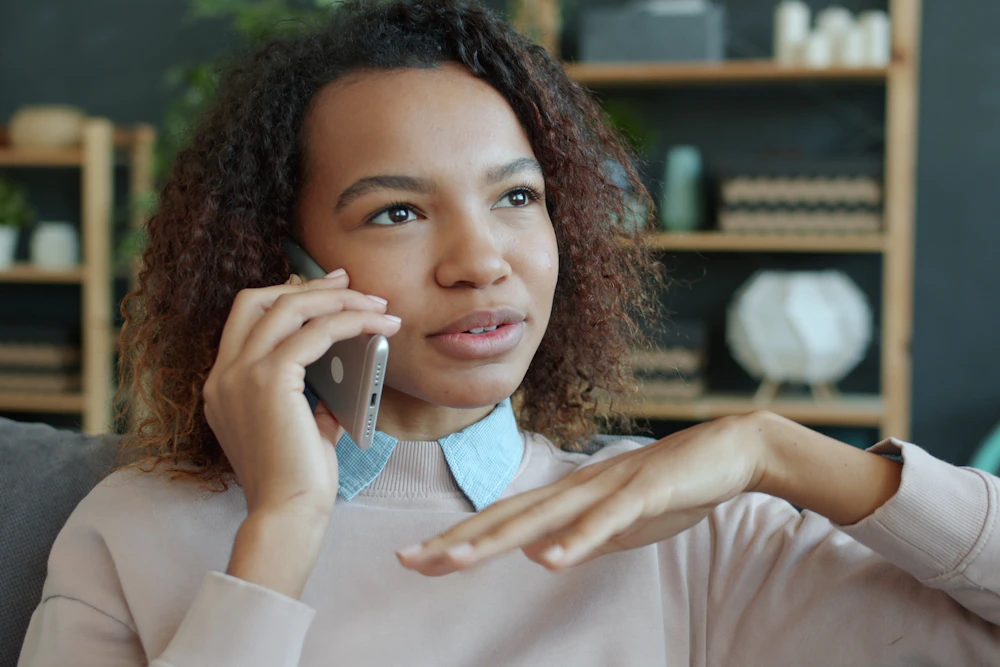 自宅のソファでスマートフォンを耳にあてて話す女性