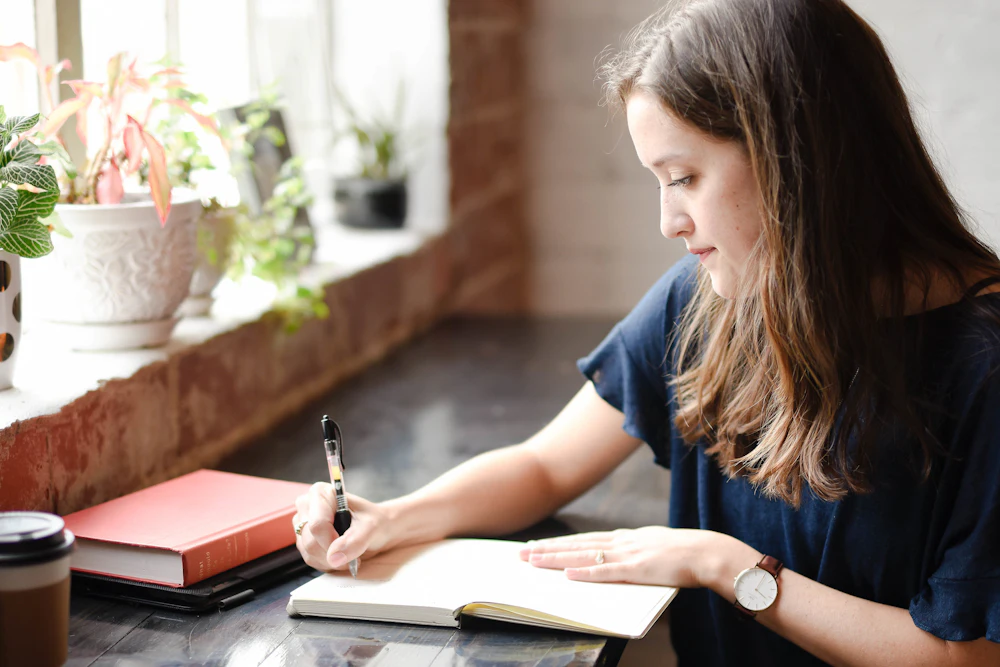 窓辺のテーブルでノートに書きこむ女性