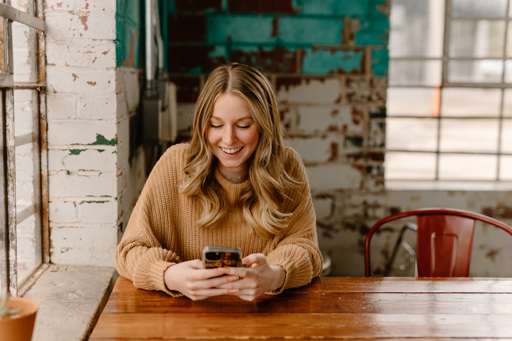 テーブルでスマートフォンを見ながらほほえむ女性